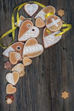  Sarı kurdeleli kalp şeklinde makro zencefilli kurabiye, ahşap arka planda çiçekler.