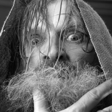 Kırmızı gömlek stüdyosunda uzun sakallı, bıyıklı ve ıslak sarı saçlı kutsanmış birinin yakın plan portresi.