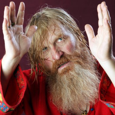 Kırmızı gömlek stüdyosunda uzun sakallı, bıyıklı ve ıslak sarı saçlı kutsanmış birinin yakın plan portresi.