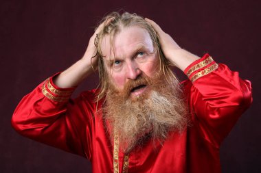 Kırmızı gömlek stüdyosunda uzun sakallı, bıyıklı ve ıslak sarı saçlı kutsanmış birinin yakın plan portresi.