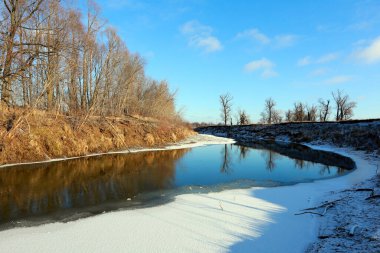 Güneşli bir kış günü, dondurucu nehrin ve yapraksız meşe ağaçlarının resimsel manzarası.