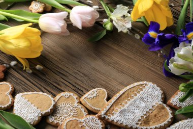  Sarı kurdeleli kalp şeklinde makro zencefilli kurabiye, ahşap arka planda çiçekler.