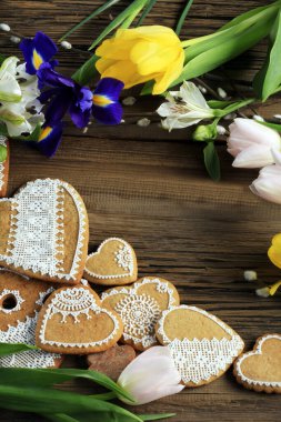 Sarı kurdeleli kalp şeklinde makro zencefilli kurabiye, ahşap arka planda çiçekler.
