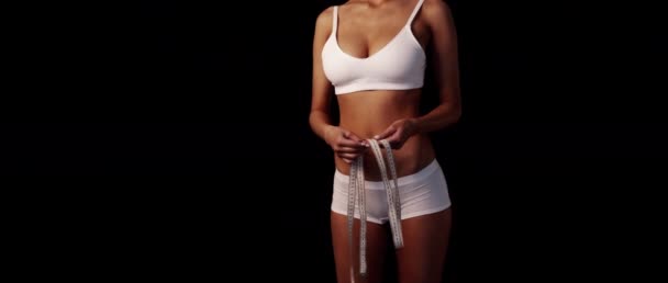 Sıska sporcu kız beyaz iç çamaşırlarıyla bronzlaşmış vücudu ölçer. Kalça ölçüleri, sağ arka planda siyah metin alanı. — Stok video