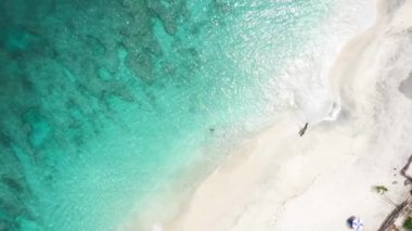 Çerçevenin ortasındaki güzel mavi gök mavisi suyun üst görüntüsü. Bir kız sıcak suyun tadını çıkarıyor. Etrafı beyaz kum ve tropikal bitki örtüsüyle çevrili.