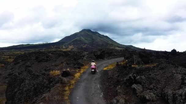 スクーターの冷却溶岩フィールドで火山のふもとに焦土の上を旅し 一人で道路に沿って2人乗り — ストック動画