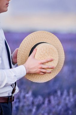 Young man, a groom in a white shirt, holds a straw hat in his hands close-up. Vertical photo while traveling in France