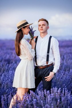 Attractive longhaired young woman in straw hat take a rest with her handsome boyfriend looking on him in scenic lavender field. Vertical photo in Provence, France