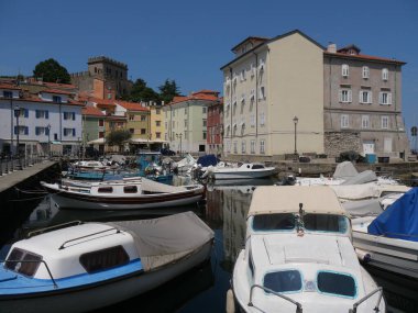 Muggia 'daki Mandracchio: köyün içinde küçük bir limandır ve antik duvarlar ve renkli binalarla çevrilidir. Suya demirlenmiş ve yansıtılan renkli tekneler var..