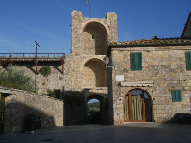 Monteriggioni 'deki Piazza Roma' da Santa Maria Assunta kilisesi ve bir kuyu ve arkasında Porta Romea olan duvarlar.