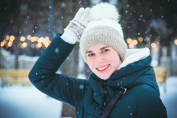 Young girl with blue eyes smiling raising her hand against the background of snowfall and city lights on a winter day