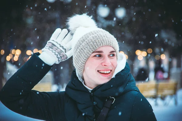 Young girl with blue eyes smiling raising her hand against the background of snowfall and city lights on a winter day