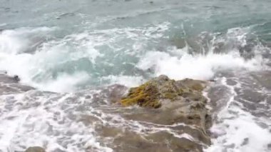 Deniz dalgaları kıyıya yakın kayalara çarpıyor.