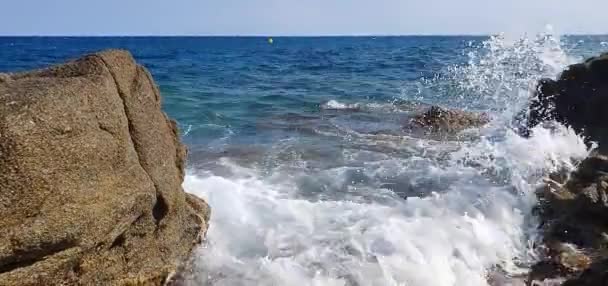 Tengeri hullámok ütköznek kövek a parton tiszta kék ég a háttérben — Stock videók