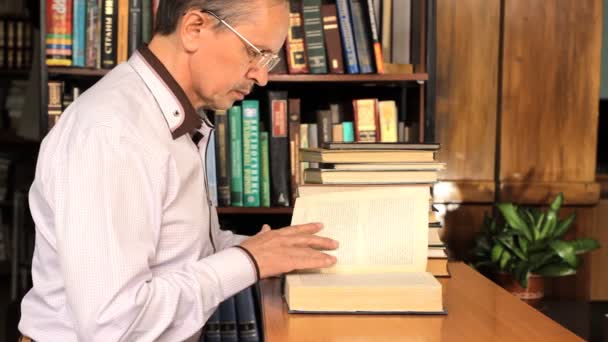 Hombre investigando con un libro en una biblioteca — Vídeos de Stock