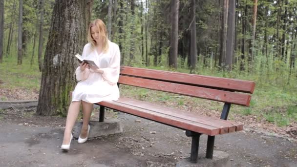 Ragazza si siede su una panchina con un libro — Video Stock