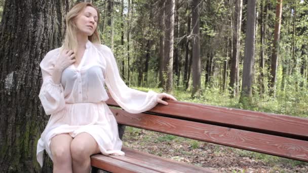 Beautiful Girl is sitting on the bench in a park and smiling — Stock Video