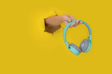 Sarı kağıt üzerinde mavi kulaklıkları tutan el. Müzik Konsepti