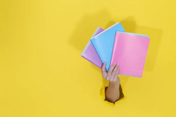 Női kéz kezében színes jegyzetfüzetek sárga szakadt papírból. — Stock Fotó