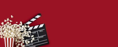 Kırmızı arka planda patlamış mısır ve el çırpma tahtası olan bir film izliyorum. Sinemaya gidenler aksesuarlar, sinematografi konsepti. Kopyalama alanı olan uzun geniş afiş
