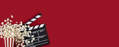 Watching movie with popcorn and clapperboard on red background. Movie goers accessories, cinematography concept. Long wide banner with copy space clipart
