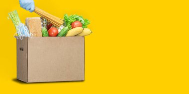 Sarı arka planda yiyecek olan bağış kutusu. Coronavirus yemek teslimatı. Gönüllü bir kutu yiyecek getiriyor. Gönüllü yiyecek topluyor. Renk Ağacı 2021 Aydınlatıcı Sarı. Kopyalama. Geniş biçim pankartı