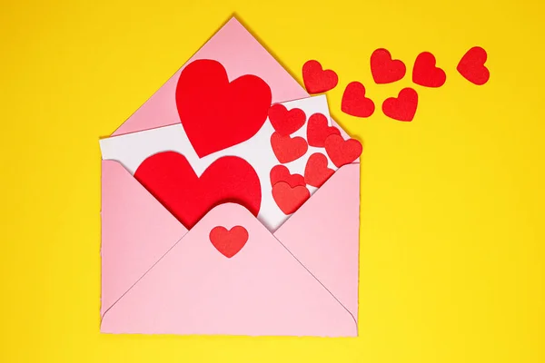 Valentinstag Karte. Papierrote Herzen fliegen aus einem rosafarbenen Papierumschlag auf gelbem Hintergrund. Papierkunst am Valentinstag. lizenzfreie Stockfotos