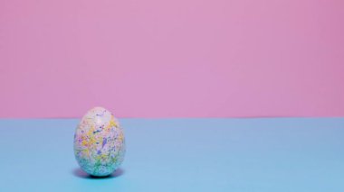 Renkli boyalı Paskalya yumurtaları yuvarlanır ve birbirlerini mavi ve pembe arka planda vururlar..