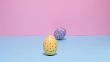 Renkli boyalı Paskalya yumurtaları yuvarlanır ve birbirlerini mavi ve pembe arka planda vururlar..