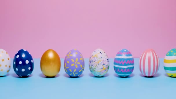 Colorful painted Easter eggs roll and knock each other on a blue and pink background. — Stock Video