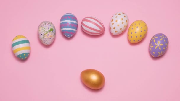 Video de Feliz Pascua. Coloridos huevos de Pascua pintados ruedan y se golpean unos a otros sobre un fondo rosa. — Vídeo de stock