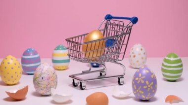 Renkli Paskalya yumurtalı alışveriş arabası. Pembe arka planda boyanmış yumurtalar.