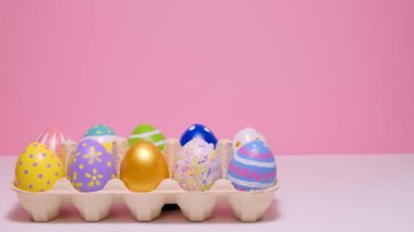 Karton bir kutuda renkli Paskalya yumurtaları. Pembe arka planda yumurtalar.