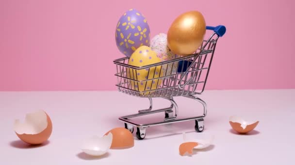 Carrito de compras con coloridos huevos de Pascua. huevos pintados sobre un fondo rosa. — Vídeo de stock