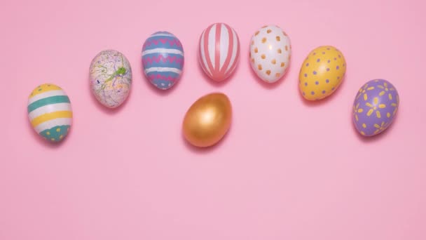 Coloridos huevos de Pascua ruedan y se golpean unos a otros sobre un fondo rosa. — Vídeo de stock