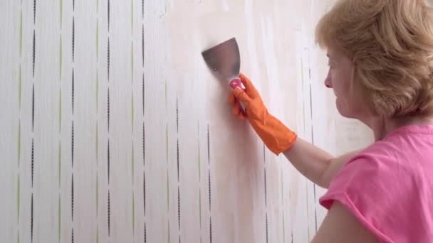 En vuxen kvinna tar av tapeten arbetar med en spatel i rummet. — Stockvideo