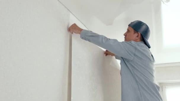4K. Mężczyzna nakładający rolkę tapety na ścianę, wygładza świeżo wklejoną tapetę — Wideo stockowe
