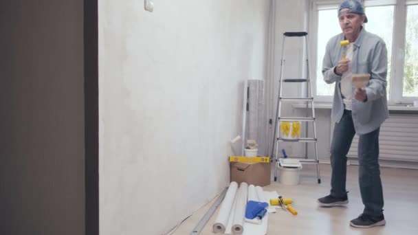 Hombre positivo bailando y cantando en un rodillo de goma que se divierte durante la reparación del hogar — Vídeos de Stock