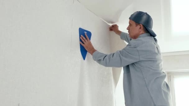 Człowiek ze szpatułką wygładzającą tapetę na ścianie. Renowacja mieszkania. — Wideo stockowe