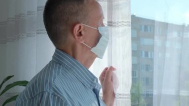 Kendini izole etmiş yaşlı bir adam evin penceresinden sokağa bakıyor.