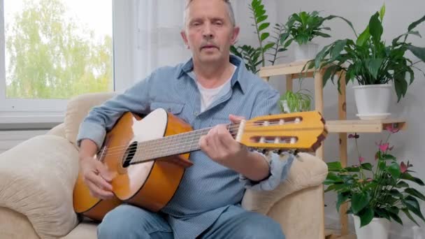 Hombre mayor toca la guitarra acústica y canta en la sala de estar apartamento — Vídeo de stock