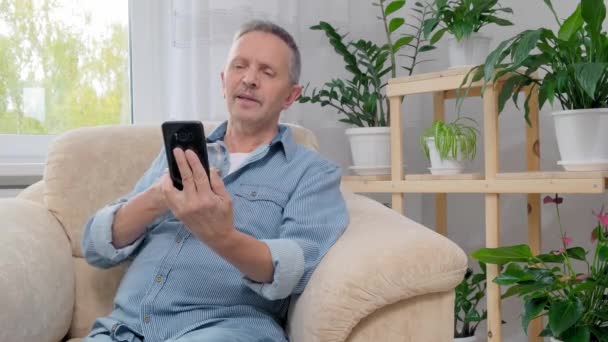 4k. Senior man while sitting on armchair holding a glass of alcohol — Stock Video