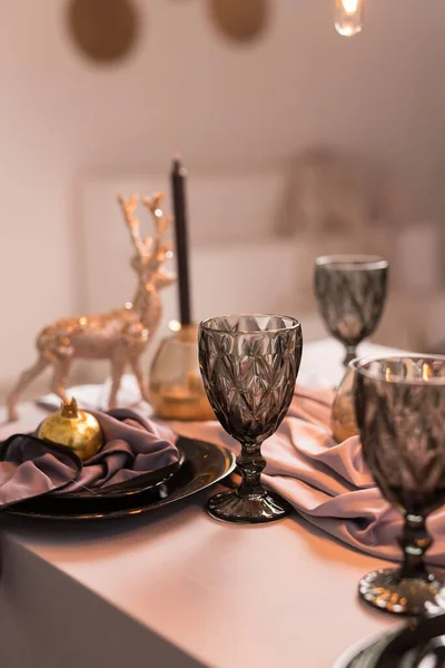 Sluiten van feestelijke kersttafel setting met lege wijnglazen en zwarte plaat met gouden granaat — Stockfoto