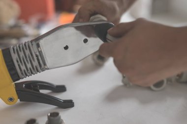 Adam polipropilen için demir lehimlemeye devam ediyor. Sarı ütülü el ve ısıtma için borularla yan görünüm