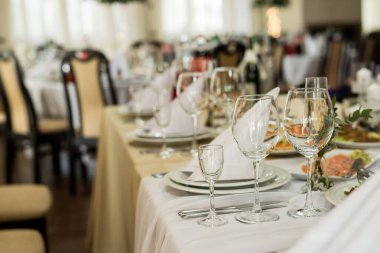 Şarap kadehleri ve bej masa örtüsünün üzerindeki taze çiçeklerle şenlik masasını kapatın.