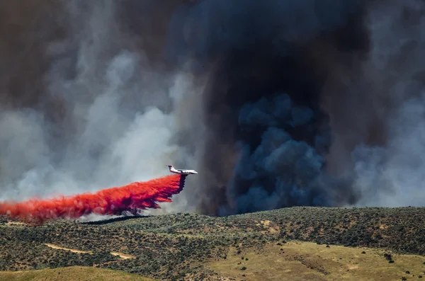 Aviones blancos dejando caer el fuego retardante, ya que combate el fuego salvaje furioso Imágenes de stock libres de derechos