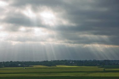 Almanya 'nın kuzeyinde Schleswig-Holstein eyâletinde Kiel yakınlarındaki tarlalarla bulutların arasından geçen güzel kırsal ve güneş ışınları.