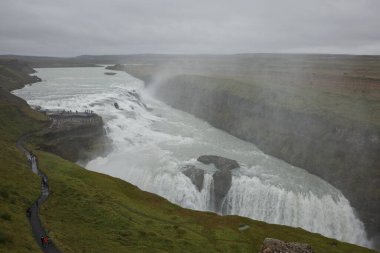 İnsanlar İzlanda 'daki Hvita nehrindeki Gullfoss şelalesinin gücünü ziyaret edip tecrübe ediyorlar..