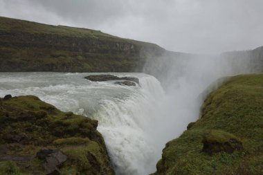İnsanlar İzlanda 'daki Hvita nehrindeki Gullfoss şelalesinin gücünü ziyaret edip tecrübe ediyorlar..