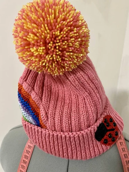 Uğur böceği ve gökkuşağı örülmüş pembe bir şapka ve ponpon